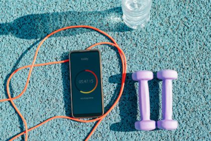 Smartphone with workout mobile app, skipping rope, dumbbells and water bottle on outdoor sports